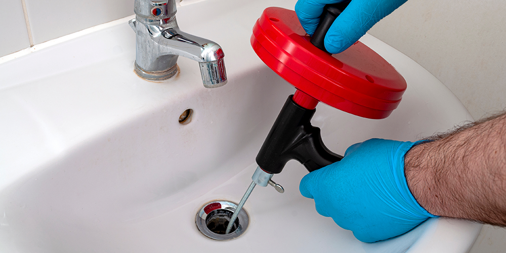 Plumber in blue gloves followed drain cleaning tips to clear a clog with a snake.